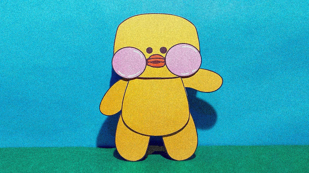 Patinho de papel Paper Duck amarelo sendo montado com tesoura, cola e papéis coloridos ao redor.