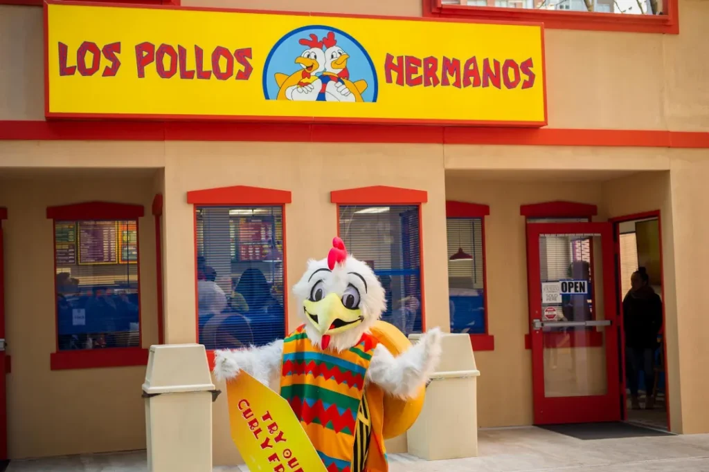 Fachada do restaurante Los Pollos Hermanos, famoso por seu frango frito, com seu mascote posando para a foto.